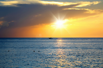 Colorful seascape image with shiny sea and speedboat over cloudy sky and sun during sunset in Cozumel, Mexico