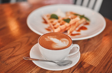 A cup of cappuccino with dessert on a wooden table