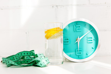 glass of water with lemon, alarm clock, measuring tape. the concept of a healthy lifestyle and...