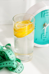 glass of water with lemon, alarm clock, measuring tape. the concept of a healthy lifestyle and weight loss