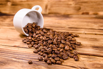White cup and scattered coffee beans on wooden table