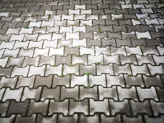 Bürgersteig mit grauem und nassem Verbundpflaster als regelmäßiges Muster in den Straßen von...