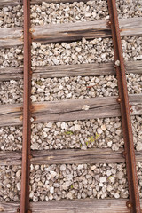 Old rusty rails on cracked wooden sleepers sprinkled with small stones. Top view of the vintage railway tracks. Closeup of part of the way