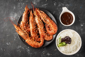 Fried grilled prawns with rice noodle, sauce and lettuce, dark background,copy space