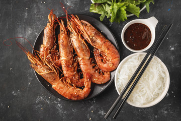 Fried grilled prawns with rice noodle, sauce and lettuce, dark background,copy space