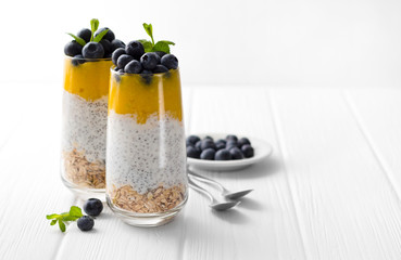 Glass of yogurt with chia seed, blueberries and mango mousse and oatmeal on a white wooden table.