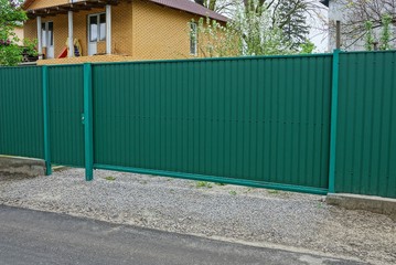 green metal gate and a fragment of a fence on a rural street