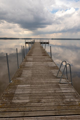 Fototapeta premium Mały mostek nad jeziorem. Odbicie chmur na powierzchni jeziora.