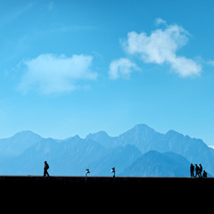 Silhouetted people walking on street over blue sky