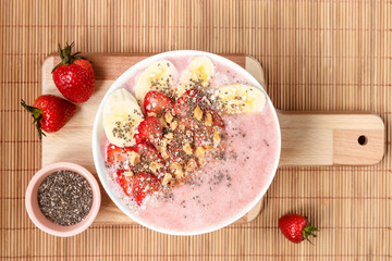 Breakfast smoothie bowl with banana, strawberries, chia seeds and cinnamon on a wooden cutting board, top view