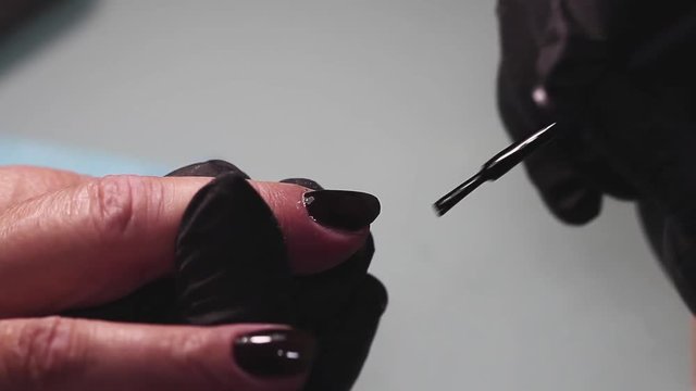 Manicure, nail lacquer, gel. The master makes a decorative manicure gel with a varnish. dark blue color of varnish, tight blue tone. Hands close-up, against the background of a yellow towel