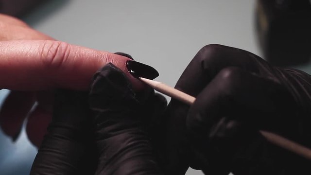 Manicure, nail lacquer, gel. The master makes a decorative manicure gel with a varnish. dark blue color of varnish, tight blue tone. Hands close-up, against the background of a yellow towel
