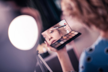 Blonde young woman looking into mirror while using eye shades