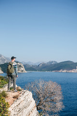 A tourist with a backpack on top of a cliff or hill next to the sea looks into the distance. Travel alone.