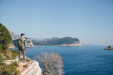 A tourist with a backpack on top of a cliff or hill next to the sea looks into the distance. Travel alone.
