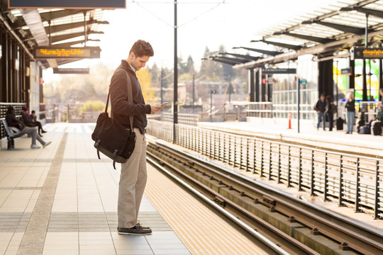 Young professional man commuter with cell phone waiting on train station platform