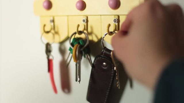 A male hand is hanging keys on a hook on the wall of a house. Selective focus