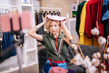 Blonde stylist showing stylish pink beret while filming blog