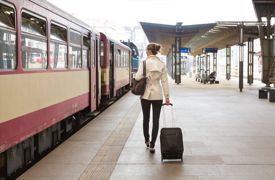 Young woman traveler with roller bag suitcase boarding a train at public railway station, Prague, Czech Republic