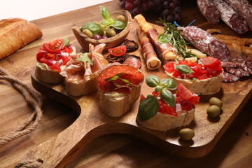 antipasto various appetizer. Cutting board with prosciutto, salami, cheese, bread and olives on dark wooden background
