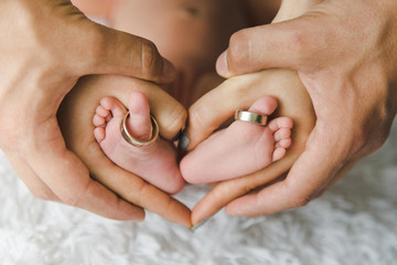 Closeup of parents hands holding newborn baby feet with wedding rings. The concept of the family.
