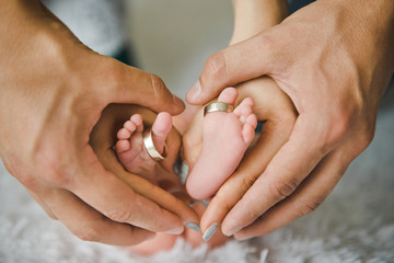 Closeup of parents hands holding newborn baby feet with wedding rings. The concept of the family.