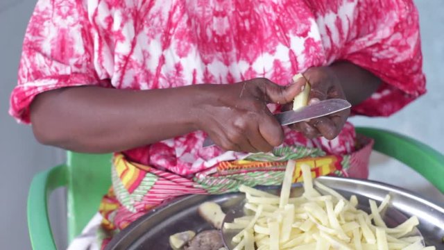 African woman sitting and cutting potato in small pieces.