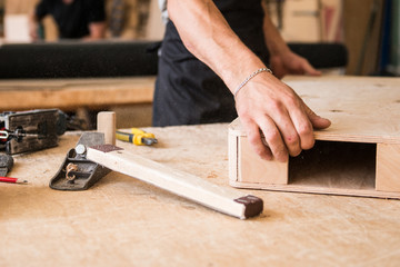 Manufacture of wooden furniture. Man carpenter builder in a gray T-shirt and working overall equals a wooden bar with a milling machine in the workshop, in the background wooden boards.
