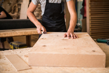 Manufacture of wooden furniture. Man carpenter builder in a gray T-shirt and working overall equals...
