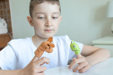 A caucasian boy playing different roles by using finger puppets, toys for expressing his emotions,...