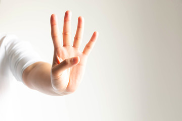 A hand showing number four in close-up on white background and little light.