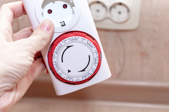24 Hour 7 days a week mains plug in timer switch european socket for energy and money saving in the hand, blurred socket on background
