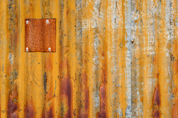 Rusty sheet of corrugated metal wall with metal patches, as an orange textured background