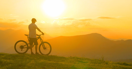 Obraz na płótnie Canvas LENS FLARE: Man rests after a bike trip and observes the evening landscape.