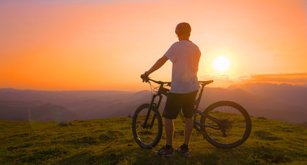 Fototapeta na wymiar SUN FLARE: Golden sunbeams shine on the mountain biker standing on top of a hill