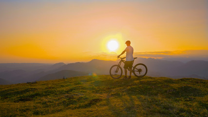 Obraz premium COPY SPACE: Bicycle rider watches the sunrise from the top of a grassy hill.