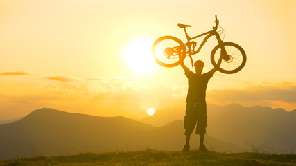 COPY SPACE: Excited man lifts his bicycle overhead after a successful journey.