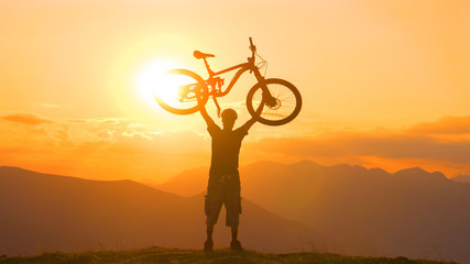 COPY SPACE: Young male cyclist holds his bicycle overhead at golden sunset.
