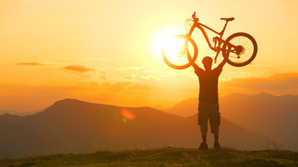 SILHOUETTE: Male tourist holds bike above head after biking up a hill at sunrise