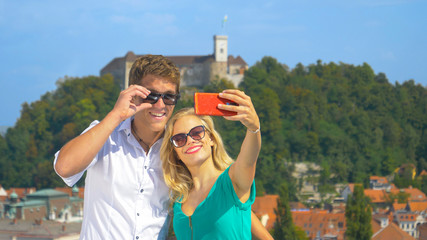 CLOSE UP: Happy girl holds up her smartphone to take a selfie with her boyfriend