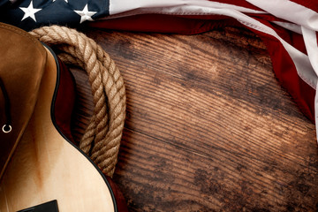 American culture, living on a ranch and country muisc concept theme with a cowboy hat, USA flag, rope lasso and acoustic guitar on a wooden background in a old saloon with copy space - obrazy, fototapety, plakaty