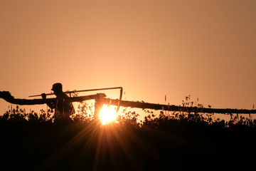 Silhouette of a Man in a village with a scythe backlight. Large manual harvesting scythe on backlight. Portrait of an man with scythe with a meadow on background. Copyspace