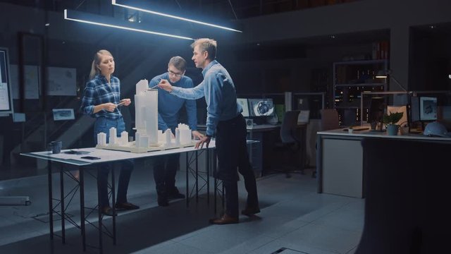 In the Creative Architectural Agency Two Professional Designers Talk with Chief Project Engineer, They Work on a Model of a City District. Urban Planners Work on a Functional Building Model.