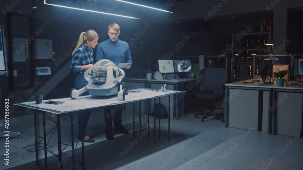 Leinwandbilder Late at Night in Robotics Engineering Facility Two Technical Engineers Talk and Work on a Wheeled Robot Prototype. In Background High Tech Research Center with Screens Showing Technology and Design