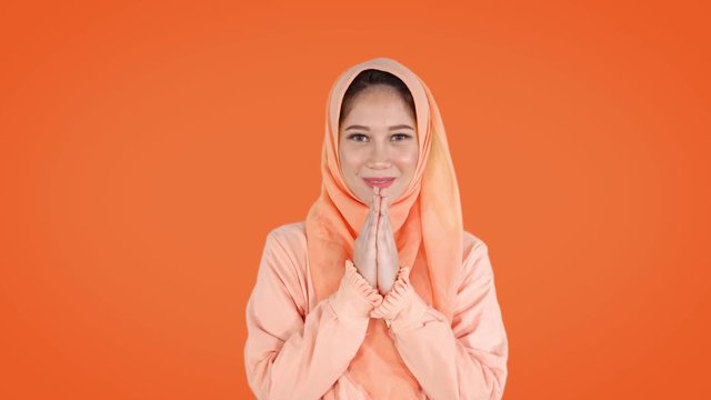 Beautiful young muslim woman wearing headscarf and showing a greeting hand gesture. Shot in 4k resolution with orange background