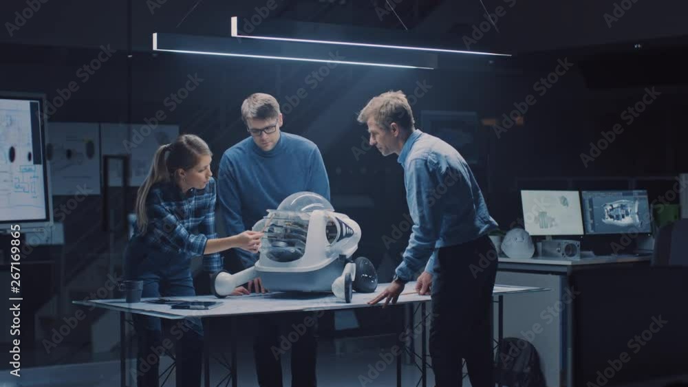 Leinwandbilder Late at Night in Robotics Engineering Facility Three Technical Engineers Talk and Work on a Wheeled Robot Prototype. In the Background High Tech Research Center with Screens Showing Industrial Design