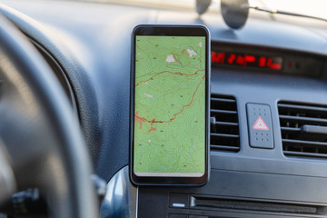 The map on the phone in the background of the dashboard. Black mobile phone with map gps navigation fixed in the mounting. App map for travel.