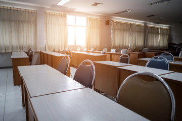 Education concept: Empty college or university classroom with wooden tables and chairs in row without student or teacher in the room. School classroom with window opened, clean and tidy ready for new 