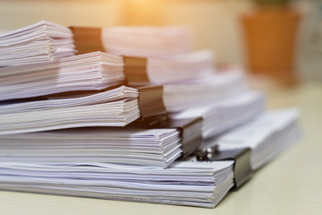 Education concept: Close and selective focus of unfinished homework assignment stack archives with binder paper clips on teacher’s desk in university waiting to be evaluated and scored. Stack of white