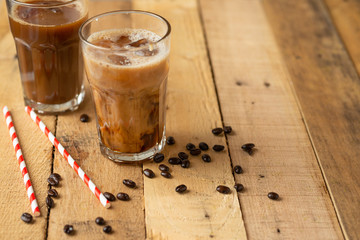 Iced iced coffee in large transparent glasses, poured over milk, with coffee beans on a wooden background, summer cooling drink, with copy space